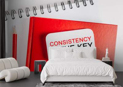 Text Consistency is the key on a white sticker on red notepad with office stationery background. Flat lay on business, finance and development concept Wall mural