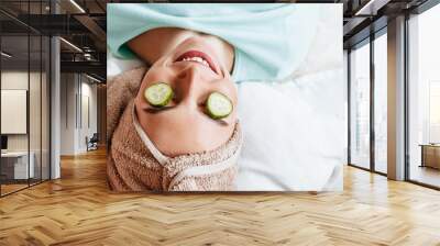 Two girls make homemade face and hair beauty masks. Cucumbers for the freshness of the skin around the eyes. Women take care of youthful skin. Girlfriends laugh at home lying on the floor on pillows. Wall mural