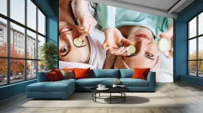 Two girls make homemade face and hair beauty masks. Cucumbers for the freshness of the skin around the eyes. Women take care of youthful skin. Girlfriends laugh at home lying on the floor on pillows. Wall mural