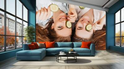 Two girls make homemade face and hair beauty masks. Cucumbers for the freshness of the skin around the eyes. Women take care of youthful skin. Girlfriends laugh at home lying on the floor on pillows. Wall mural