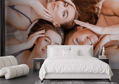 Women rest and have fun. Girlfriends laugh at home lying on the floor on pillows. Tree girls make homemade face and hair beauty masks. Women take care of youthful skin. Wall mural