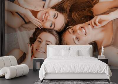 Women rest and have fun. Girlfriends laugh at home lying on the floor on pillows. Tree girls make homemade face and hair beauty masks. Women take care of youthful skin. Wall mural