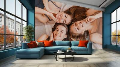 Women rest and have fun. Girlfriends laugh at home lying on the floor on pillows. Tree girls make homemade face and hair beauty masks. Women take care of youthful skin. Wall mural