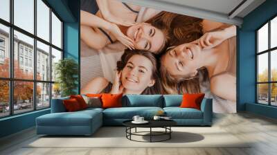 Women rest and have fun. Girlfriends laugh at home lying on the floor on pillows. Tree girls make homemade face and hair beauty masks. Women take care of youthful skin. Wall mural