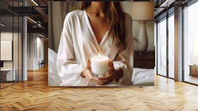 Young woman holding burning candle jar in her hands, container candle mockup closeup shot, mindfulness home interior in natural colors Wall mural