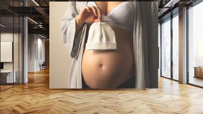 Pregnant woman holding baby cap next to her pregnant belly. Baby clothes. Maternal prenatal care. Maternity, pregnancy, baby expectation concept. Second trimester of pregnancy. Copy space Wall mural