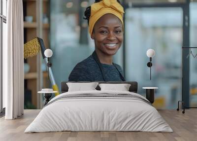 Portrait of a smiling african office cleaner in apron and gloves holding a mop while working Wall mural