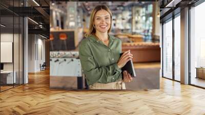 Pretty woman manager in casual clothes standing with laptop in cozy coworking and looking at camera  Wall mural