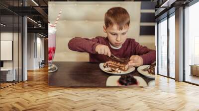 Satisfied boy of 7 years in a restaurant has a cake with a milkshake. Wall mural