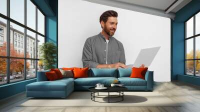 Smiling male entrepreneur working on laptop while standing on white background Wall mural