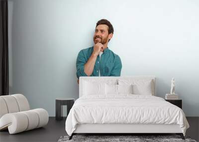 Smiling man holds his hand at his chin and looks thoughtfully aside on white background Wall mural