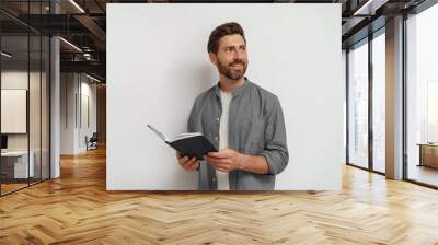 smiling man in casual clothes standing with open notepad and looking at side white background Wall mural