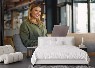 Stylish woman freelancer working on laptop in cozy coworking and looking at side Wall mural