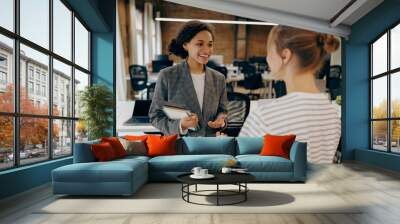 Two young diverse business women chatting during work break standing in modern office Wall mural