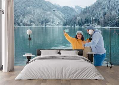 winter travel across Europe. view of the alpine lake with snow. portrait of happy family of travelers with child taking selfie on smartphone Wall mural