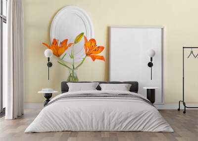 Two frames A4 and oval white frame with orange summer lily in glass vase on yellow wall background. Wall mural