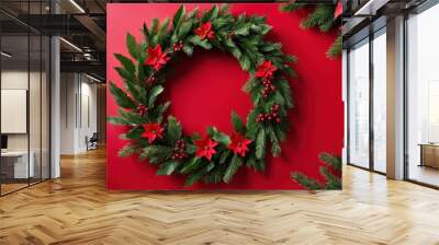 A festive wreath adorned with red flowers and greenery against a red background. Wall mural