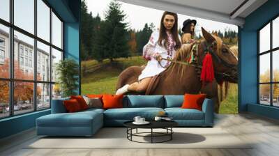 Young women ride horses in national Ukrainian dresses in the Carpathian mountains. Photo session with horses in the mountains. Ukrainian culture concept Wall mural