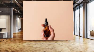 Dropper Bottle Mock-Up. Female hand holding amber glass dropper bottle on beige background Wall mural