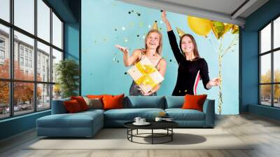 Two happy young women in birthday hats holding balloons celebrating birthday blowing confetti Wall mural