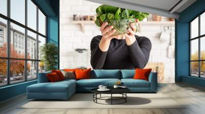 Young blond smiling woman holding a bowl of fresh spinach in the kitchen Wall mural