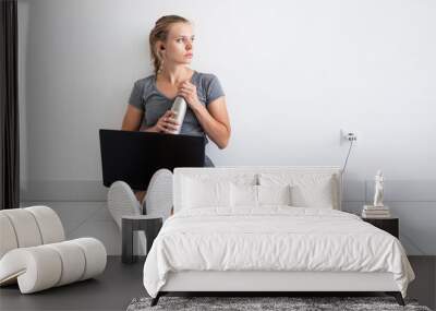 Young woman working with laptop from home, sitting on the floor and drinking water Wall mural