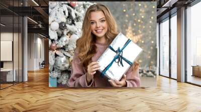 Beautiful girl in pink sweater with christmas box gift near pink and blue Christmas tree. Magical time. Wall mural