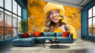 Beautiful girl walking outdoors in autumn. Smiling girl collects yellow leaves in autumn. Young woman enjoying autumn weather. Wall mural