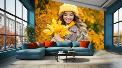 Beautiful girl walking outdoors in autumn. Smiling girl collects yellow leaves in autumn. Young woman enjoying autumn weather. Wall mural