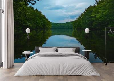 A calm lake surrounded by dense forest, with the water perfectly reflecting the trees and sky Wall mural