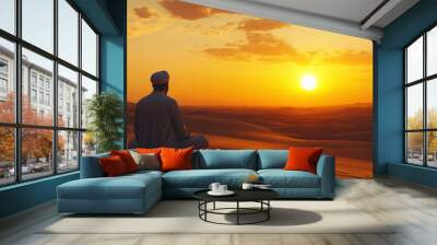 A Muslim man kneels in prayer against the backdrop of a stunning sunset in a quiet desert setting Wall mural