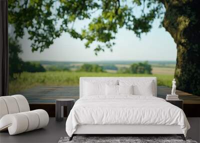 Sunlit wooden table beneath a large oak tree, overlooking a peaceful green field and distant horizon Wall mural