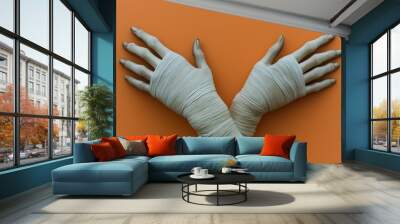 Two hands, wrapped in light bandages, gesture upward against an orange backdrop Wall mural