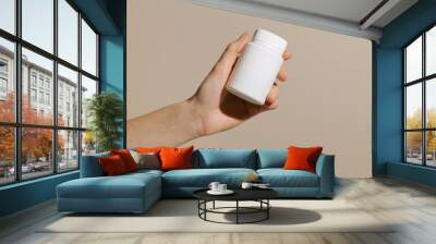 Female hand holding a white mockup jar with dietary supplement capsules on a beige background. Concept of pharmacy and medicine, health care Wall mural