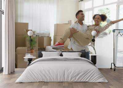 Ecstatic young couple celebrating their new home with the young man holding his wife in his arms as she grins and laughs at the camera Wall mural