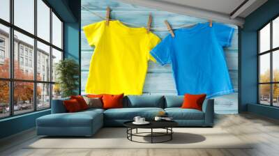 two bright baby t-shirts hanging on a clothesline on a blue wooden background Wall mural