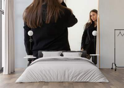 Back of young woman standing in front of mirror in black blazer and leopard print pants poses confidently in minimalist modern interior studio. Female model in fashion-forward outfit, elegant style Wall mural