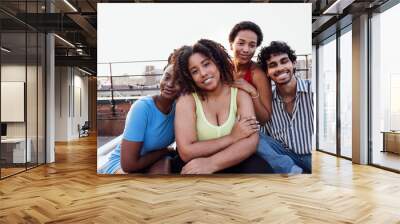 A young multi-ethnic group of smiling friends hugging each other. Portrait photo of young cheerful mixed race people looking at camera outdoors. Wall mural