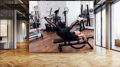 Athletic fit girl in black sportswear performs physical exercises on universal bench for training the press. Wall mural