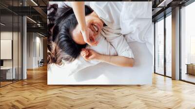 Attractive happy Asian woman lies on a white linen bed in the morning Wall mural