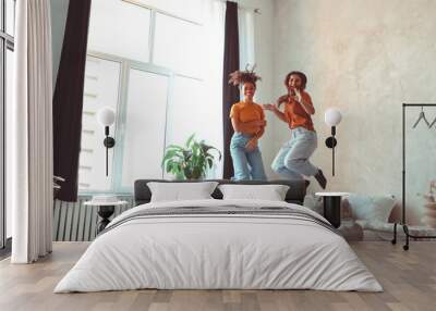 Two happy joyful girlfriends of different races jumping on bed and having fun together at home Wall mural