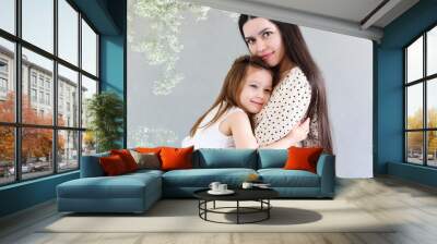 Young brunette mother and little daughter stand near the wall with big flowers wreath Wall mural