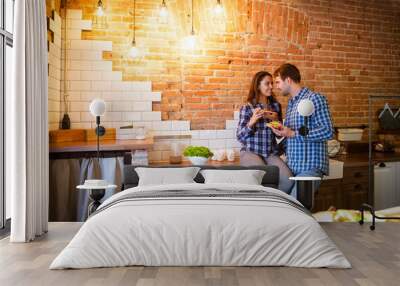 Young man and woman cooking and eating together at kitchen Wall mural