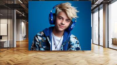 Funny cheerful teenager guy blonde with headphones listening to music on the blue background. Generative AI. Wall mural