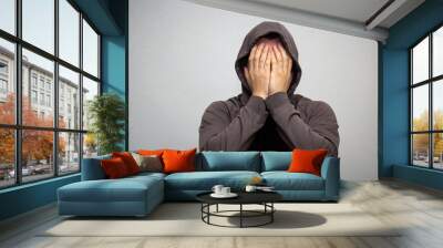 portrait of young adult man in the gray hood covered his face with his hands Wall mural