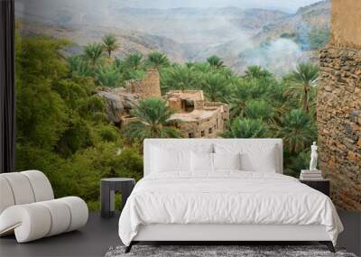 Scenic view of a traditional village nestled among palm trees in the mountains of Oman during a serene afternoon Wall mural