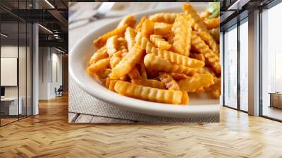 A closeup view of a plate of crinkle cut french fries, in a restaurant or kitchen setting. Wall mural