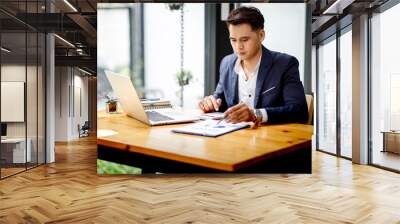 a young handsome man or businessman working on laptop computer in modern office. doing finances, acc Wall mural