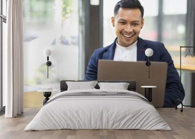 Asian Business man Using laptop computer, Successful Asian entrepreneur smiling in satisfaction as he checks information on his laptop computer while working Wall mural