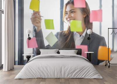 Business Asian female employee with many conflicting priorities arranging sticky notes commenting and brainstorming on work priorities colleague in a modern office. Wall mural